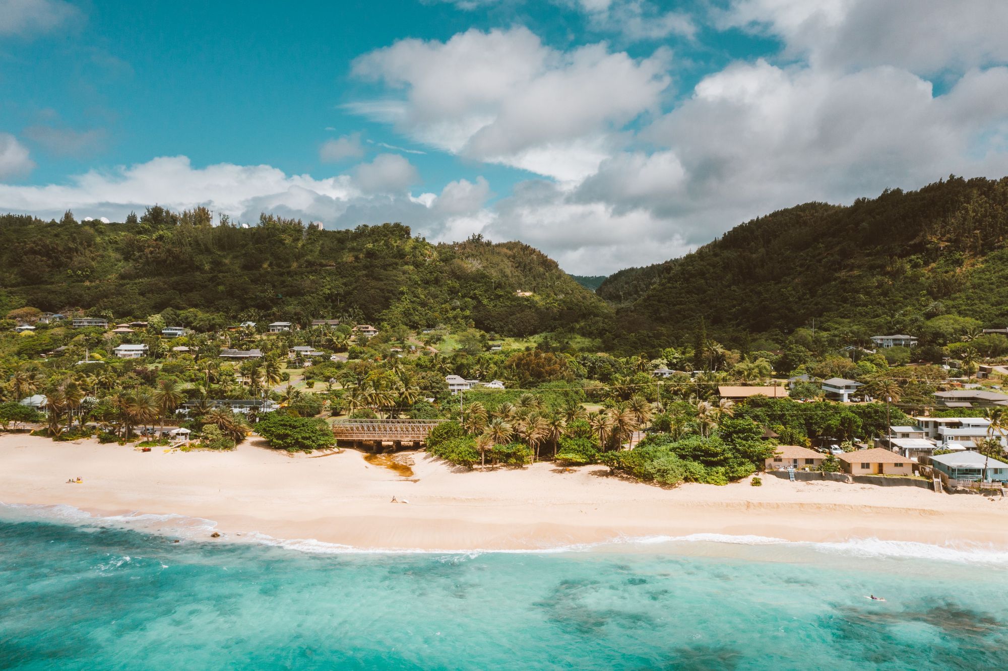 Aerial view of the Pupukea coast with a white-sand beach below green hills