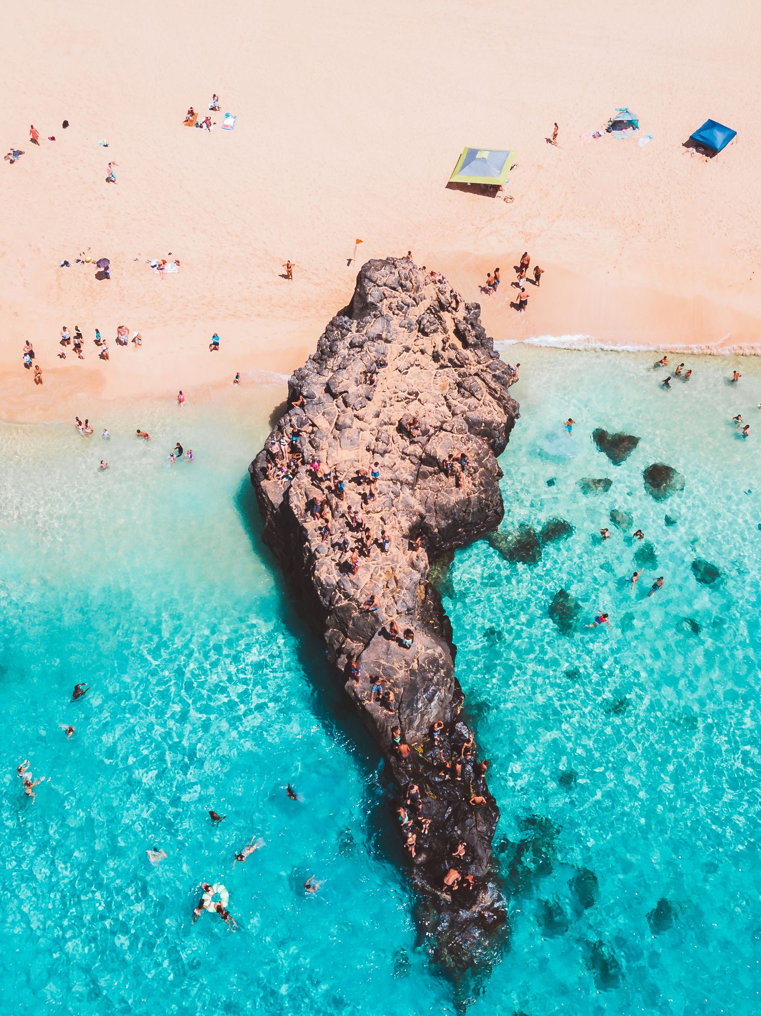 The big rock at Waimea Bay surrounded by clear turquoise water and swimmers